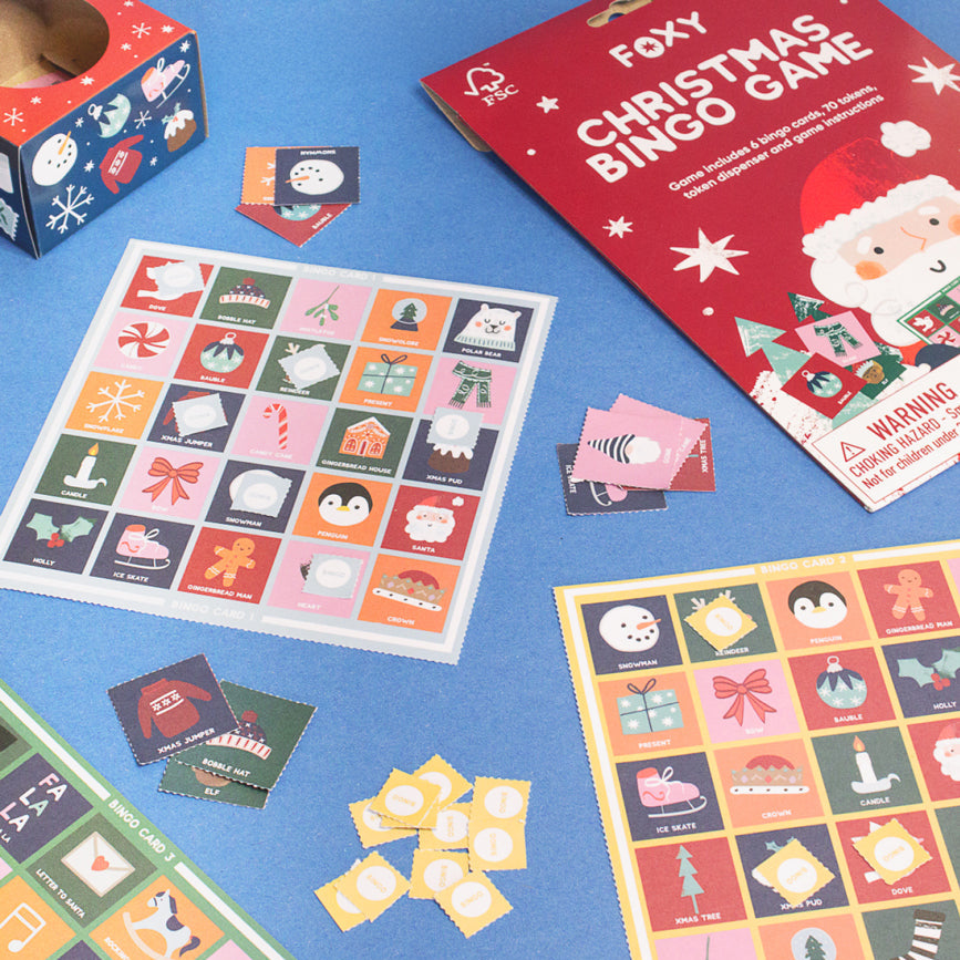 Christmas Bingo game in card, with Christmas themed illustrated pack, boards and counters laid on a blue surface