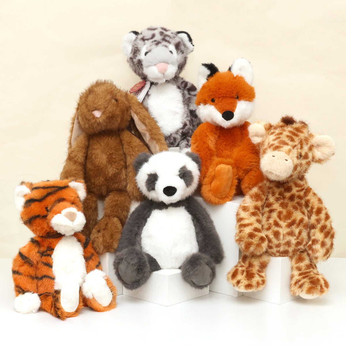 Group image of Enchanted world Eco plush collection; snow leopard, rabbit, fox, tiger, panda and giraffe shitting together facing forward in staggered heights on white surface and cream background