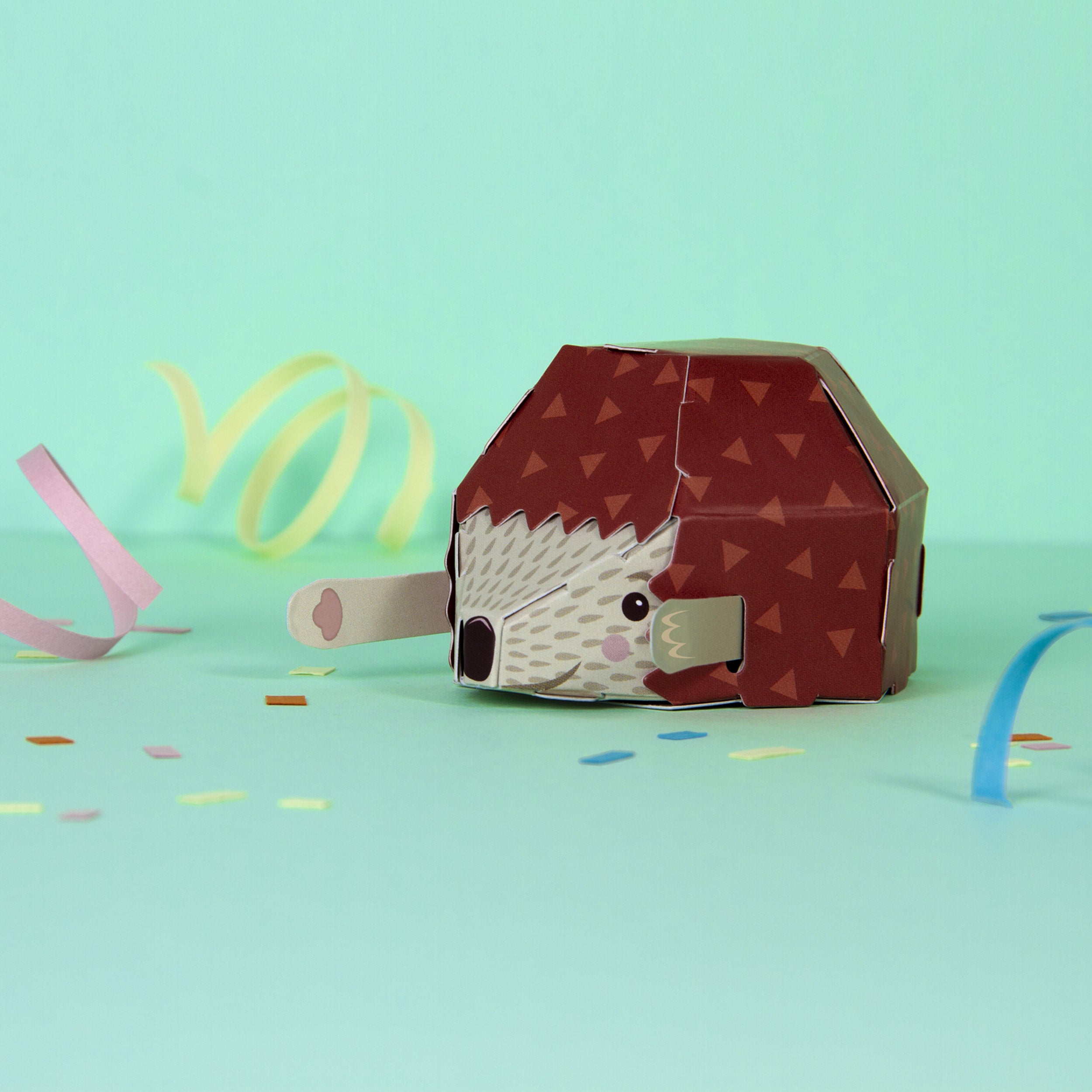 Fully assembled cardboard hedgehog on mint green background with party streamers