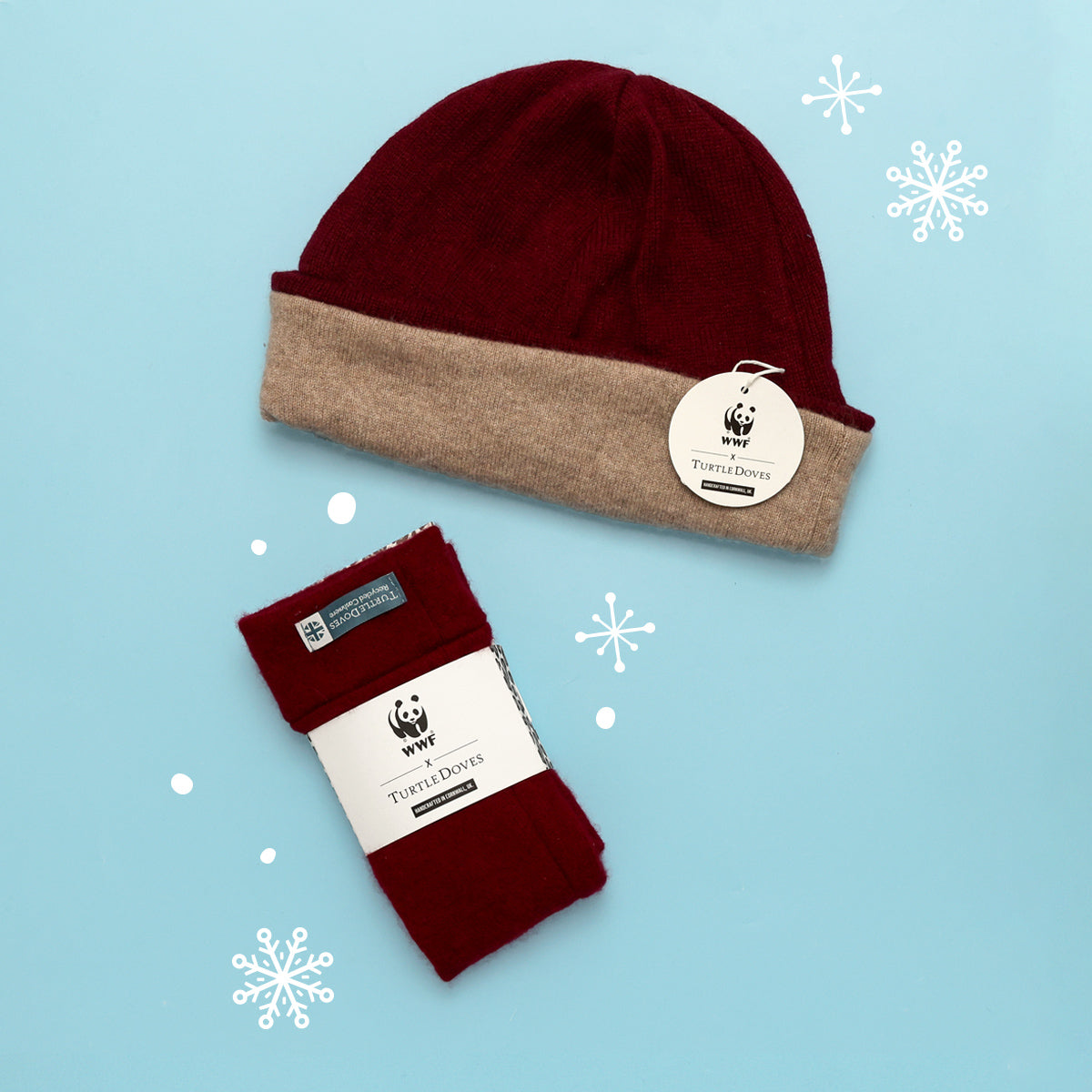 Close up of the beanie and fingerless gloves in berry, showing the co-branded WWF packaging on a blue background with white snow flake graphics