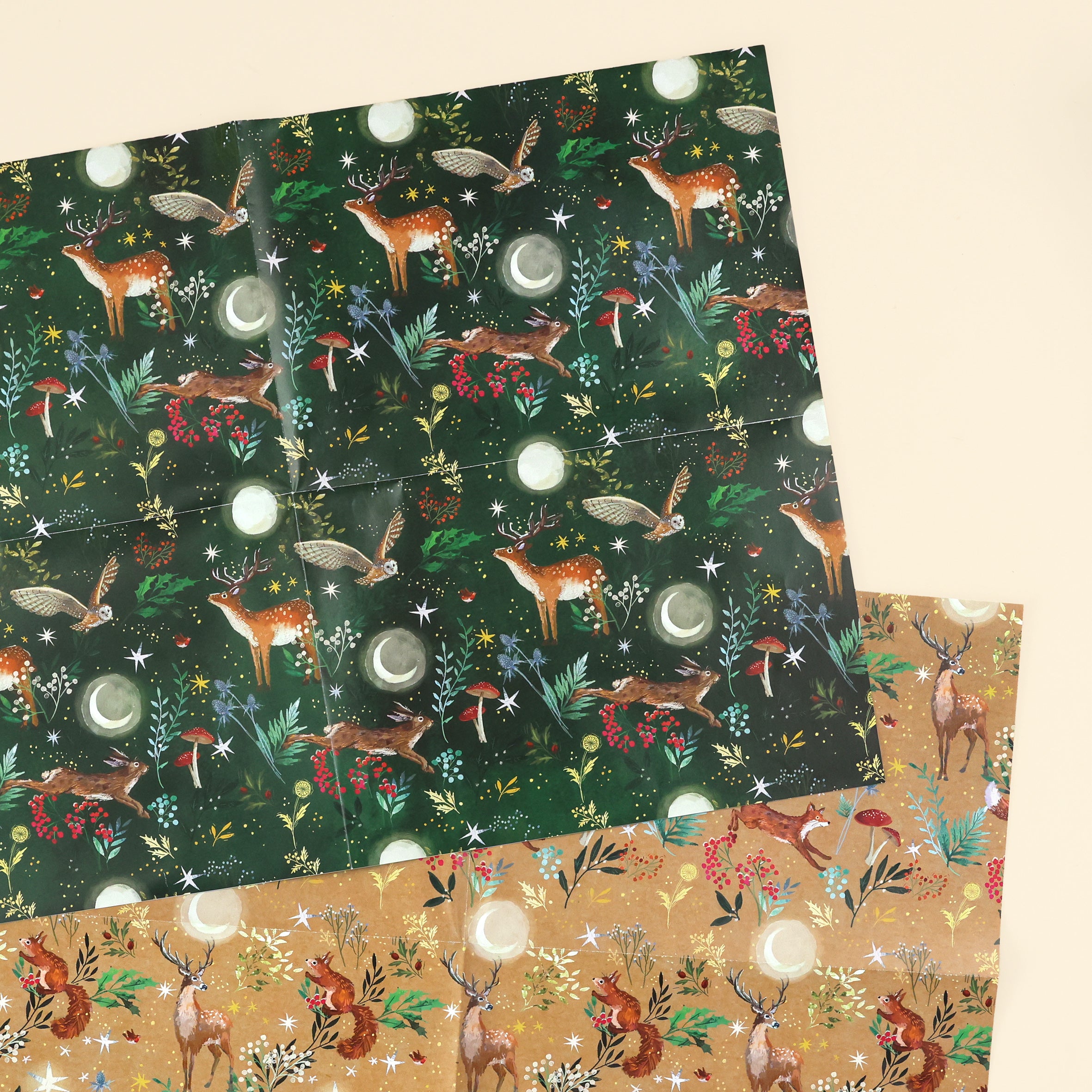 Close up of 2 woodlands designs; one with illustrated deer, owls and hare on dark green background and the other design is a fox, stag and red squirrel on a craft brown background, both in forests with plants, mushrooms, stars and moons