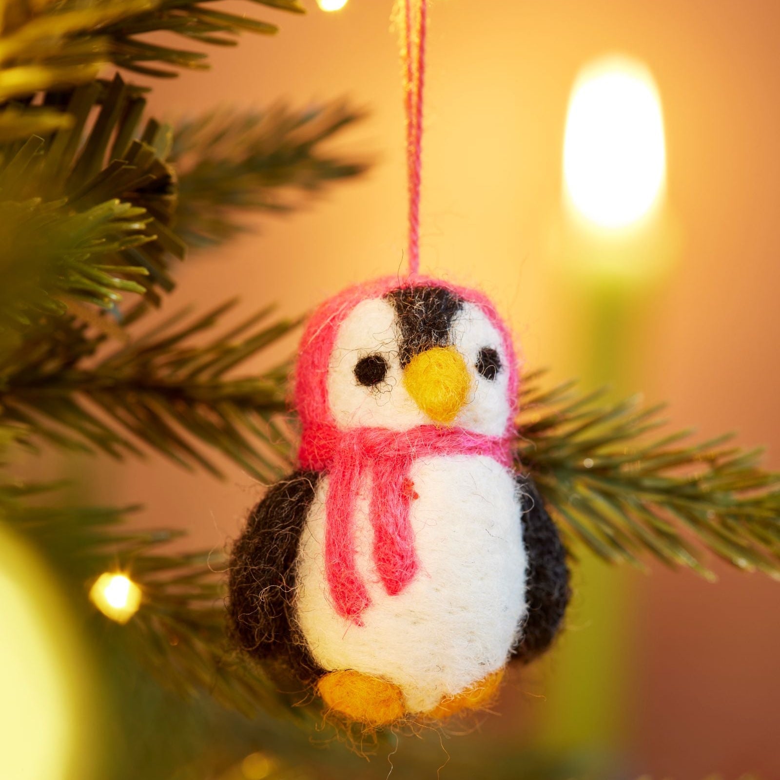 Close up of handmade felt penguin decoration with Pink hood and scarf hanging in tree with lights