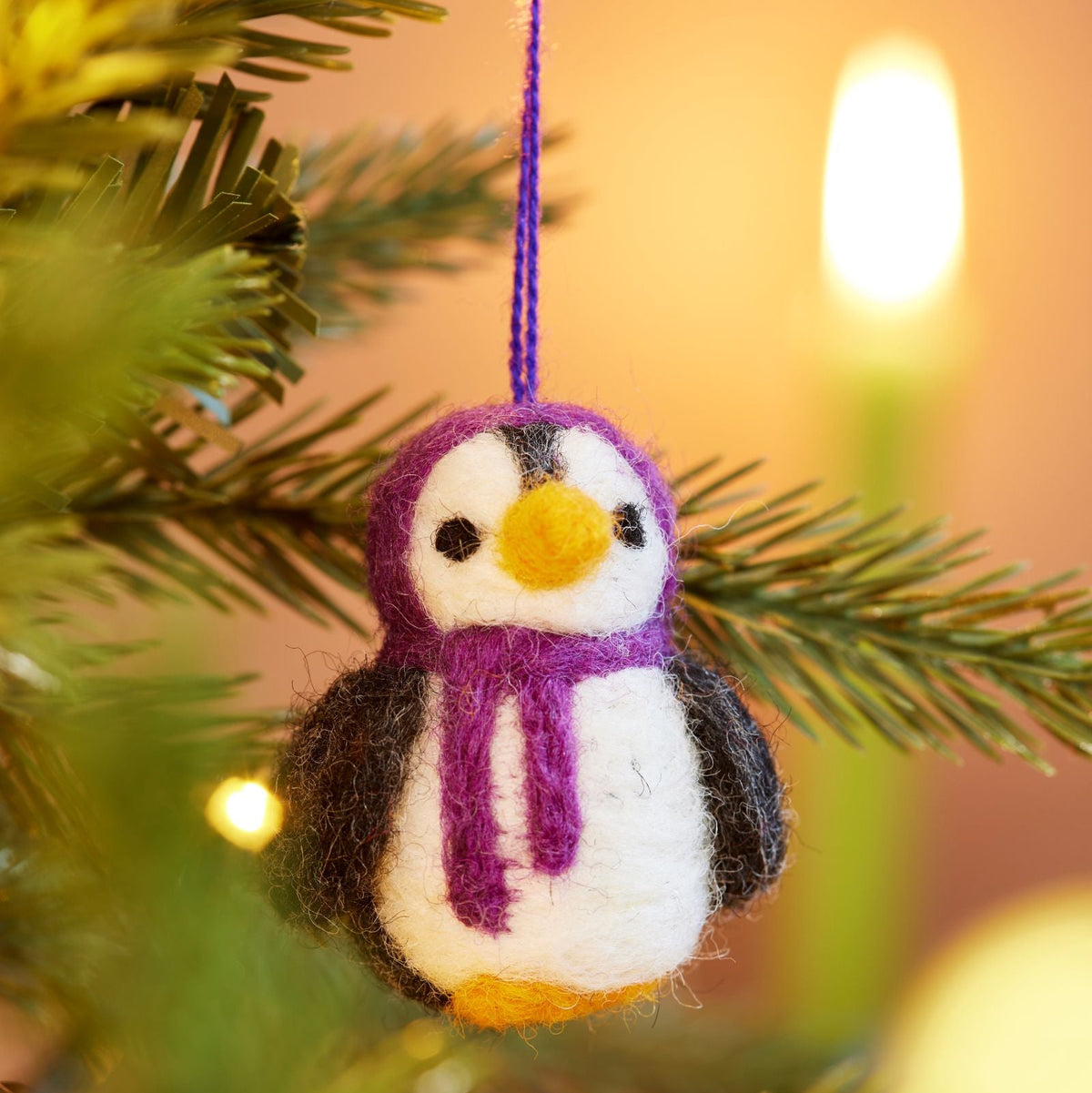 Close up of handmade felt penguin decoration with Purple hood and scarf hanging in tree with lights