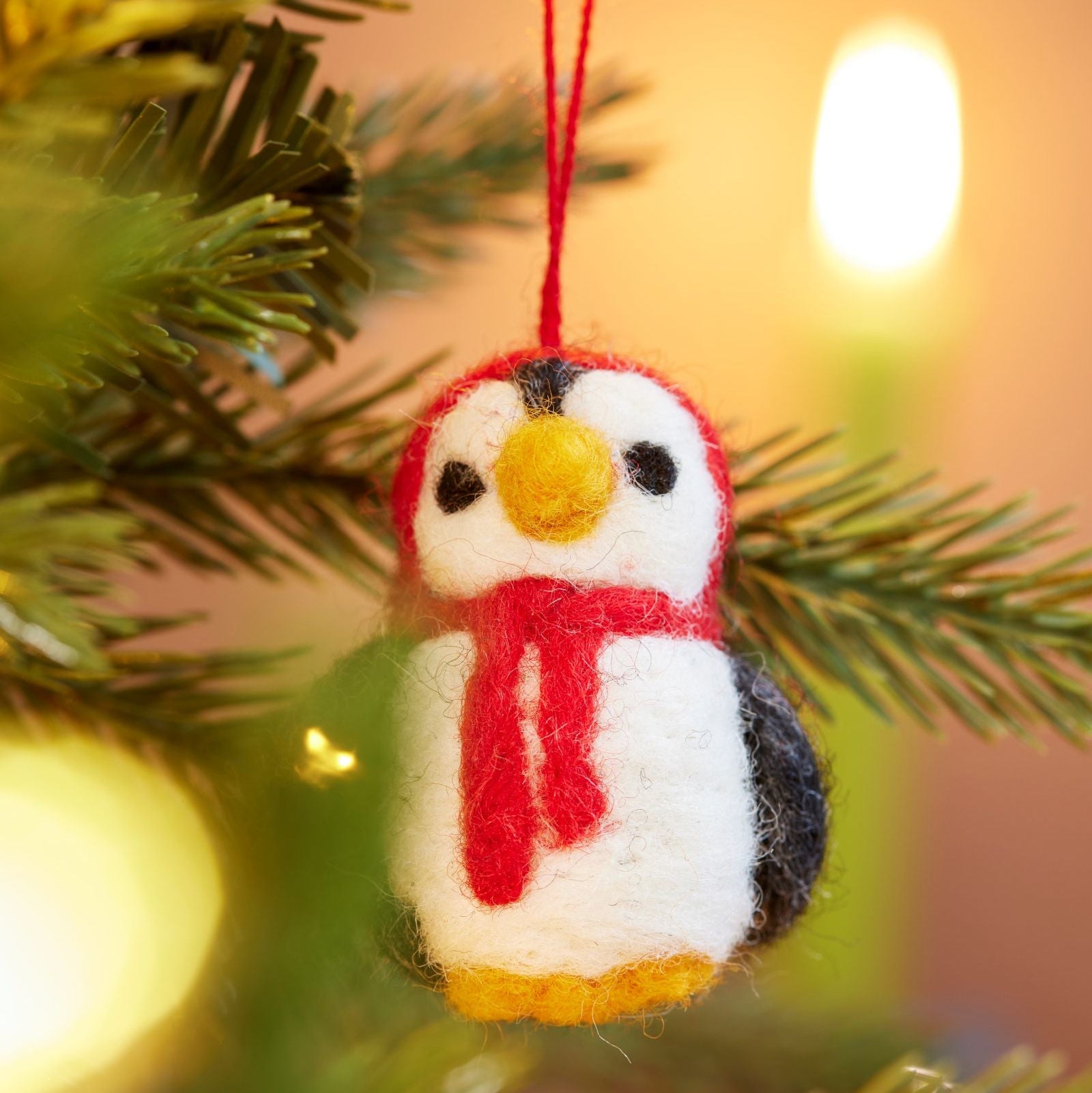 Close up of handmade felt penguin decoration with Red hood and scarf hanging in tree with lights