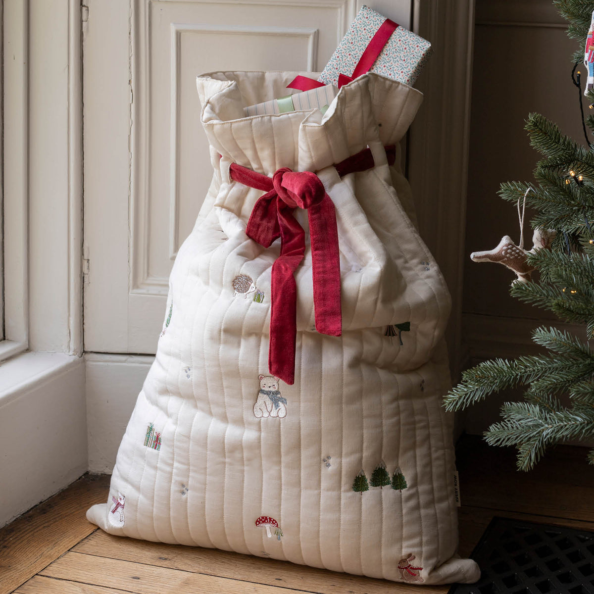 Front of embroidered Cotton present sack full of gifts and red velvet ribbon by a window