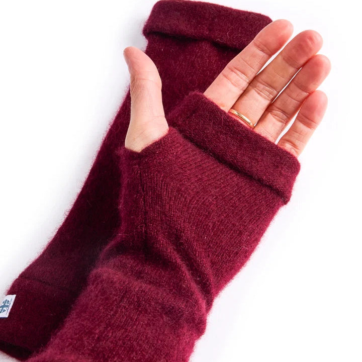 Close up of palm with recycled cashmere fingerless gloves in red being worn on white surface