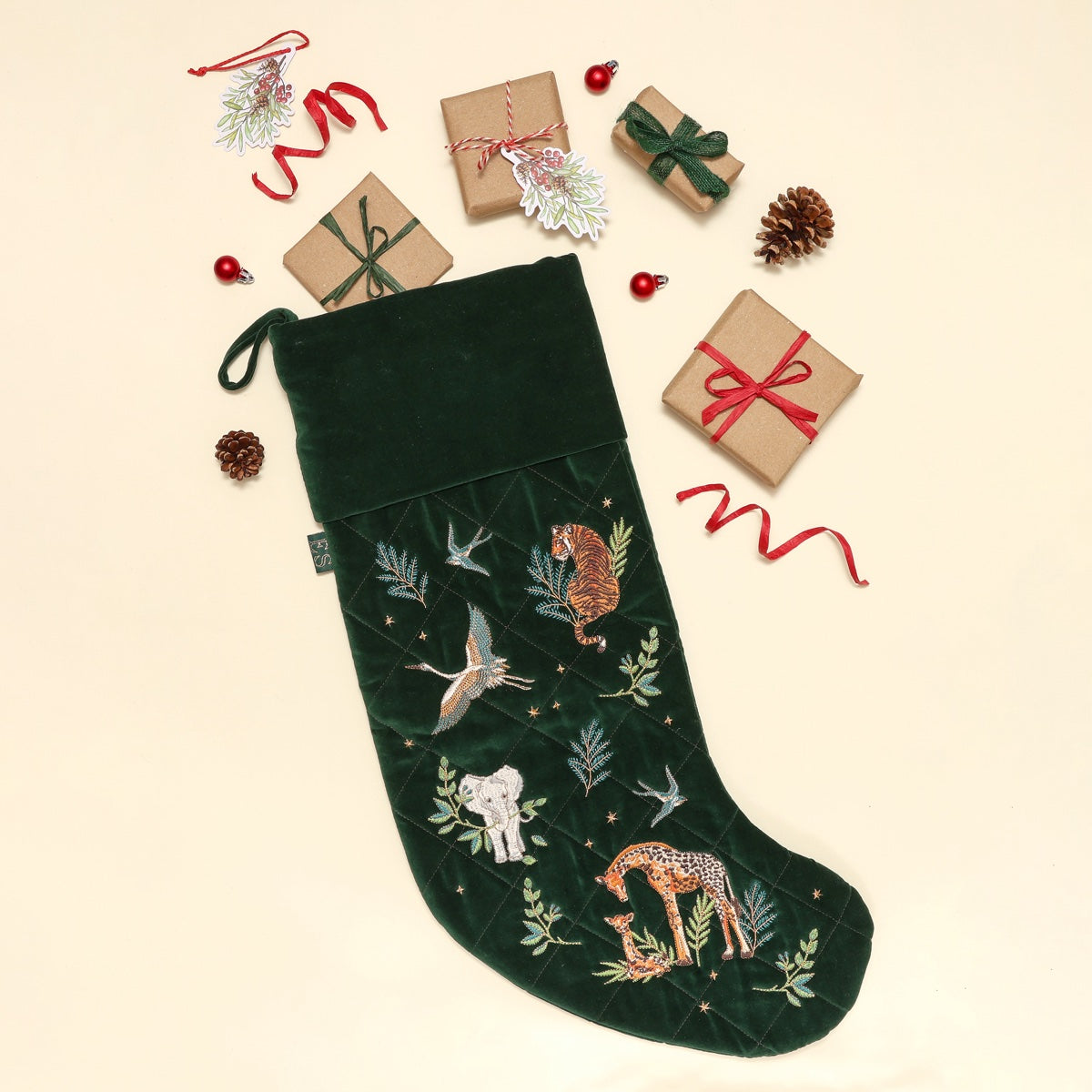 Green velvet Christmas stocking embroidered with a tiger, elephant and giraffes, surrounded by wrapped gifts