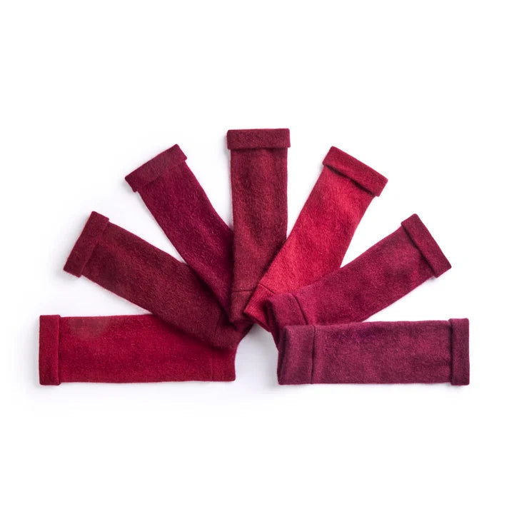 Recycled cashmere fingerless gloves in different tones of berry laid on white surface