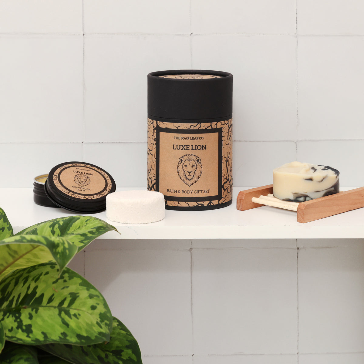 Luxe lion bath and body set on white shelf with white tiled background and plant. Showing hand soap, shower steamer and face balm in tin