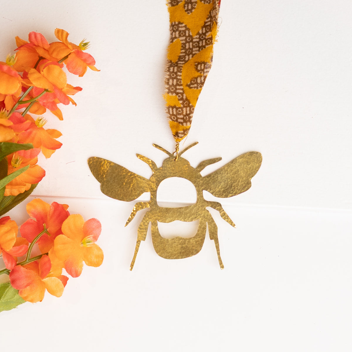 hammered brass bee decoration with recycled sari ribbon on white surface next to silk flowers
