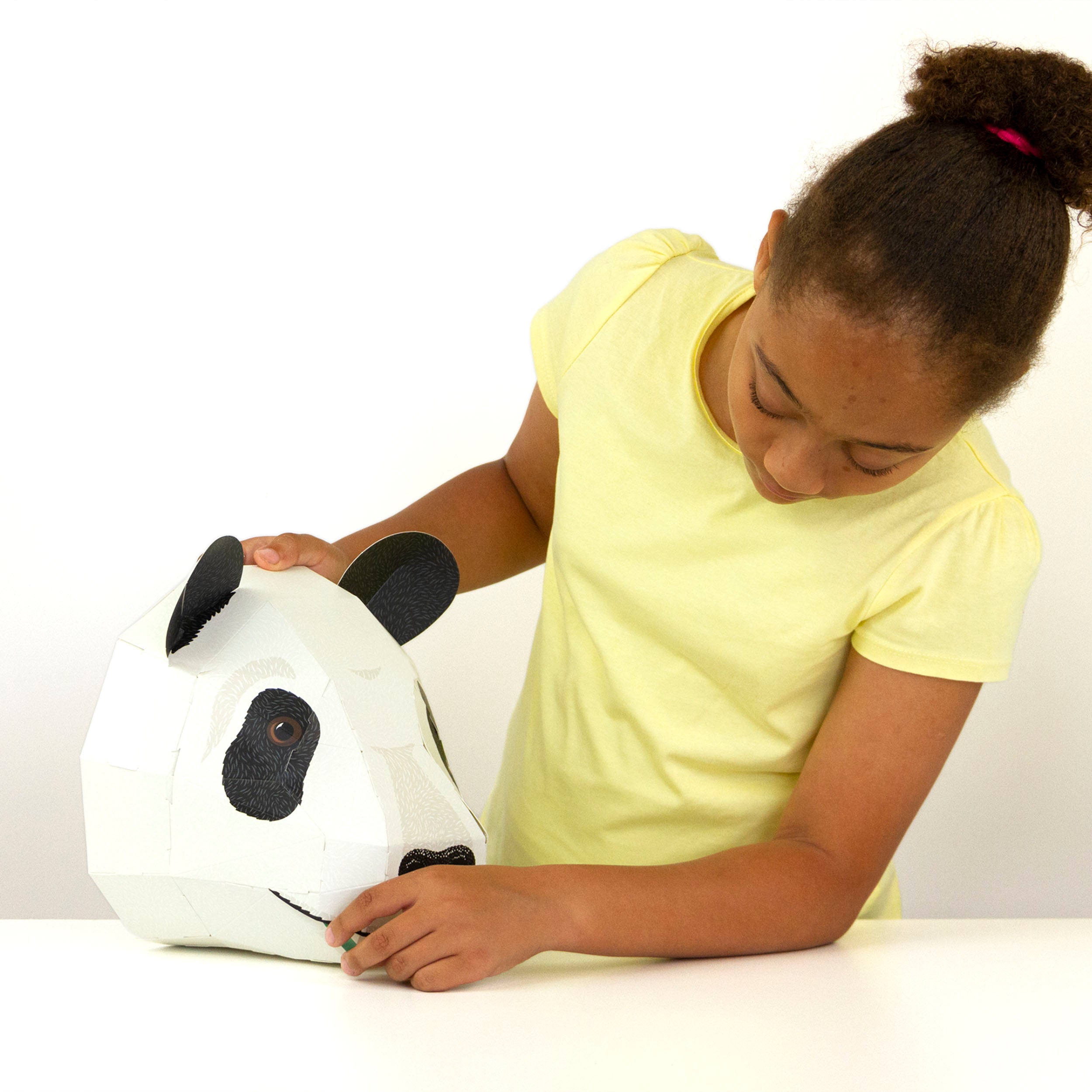 Child holding and looking at the constructed cardboard panda head on a white table