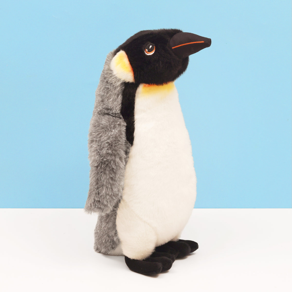 Right side of King emperor penguin made from recycled bottles standing on white surface and blue background
