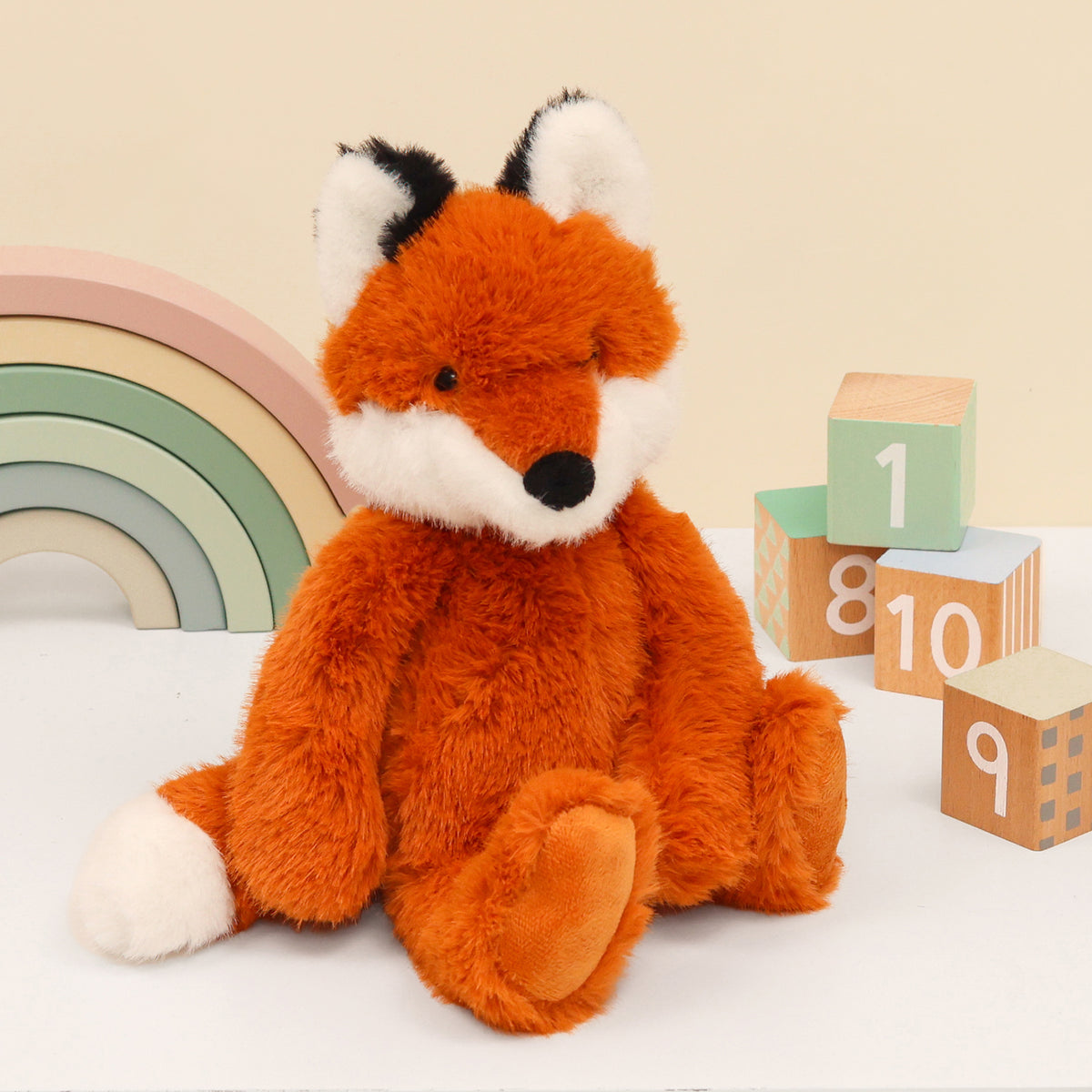 Right side of super fluffy enchanted world fox plushie in orange, with white face, ears and tail. Sitting on a white surface with wooden blocks and rainbow