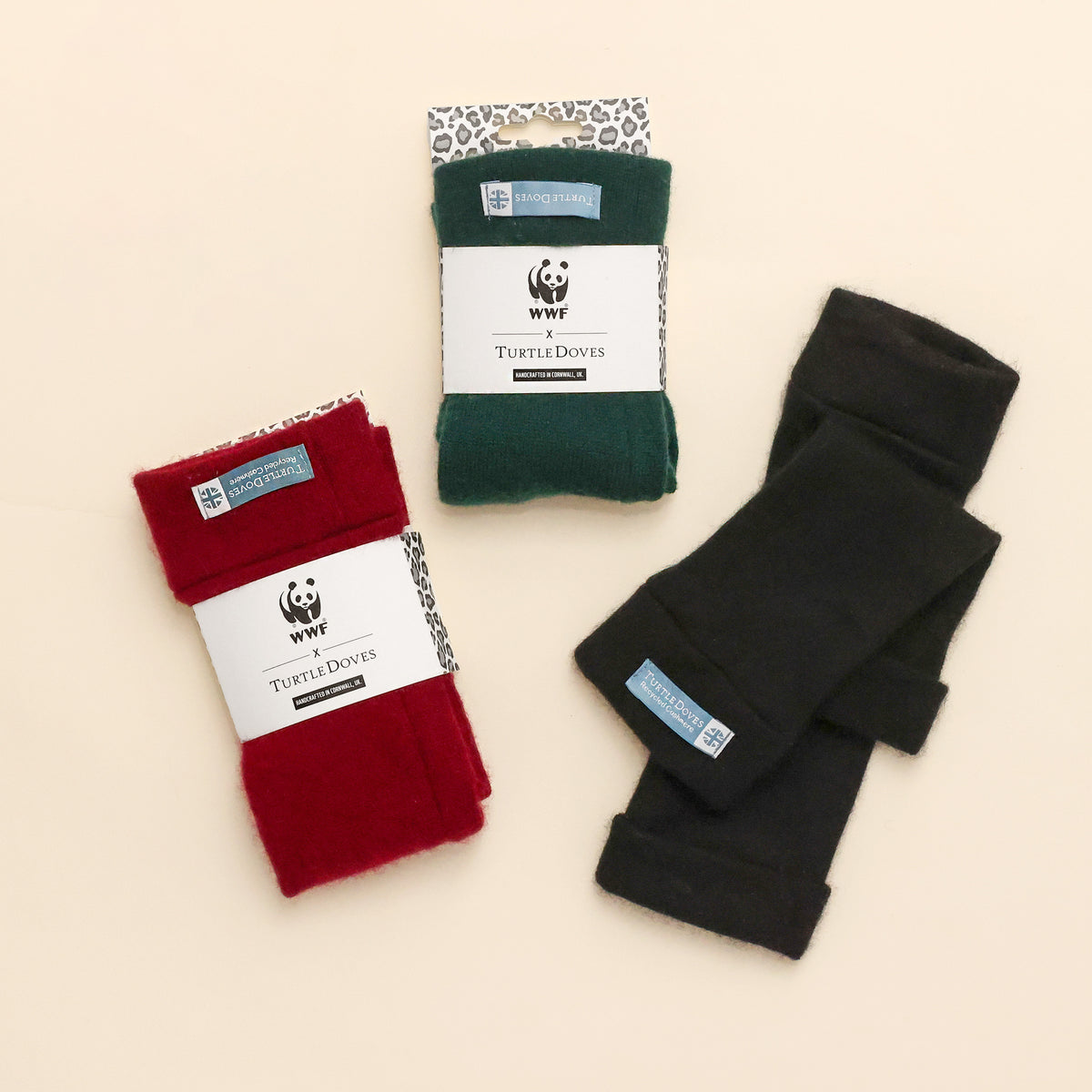 Three different options of recycled cashmere fingerless gloves in Forest green, berry and black, showing the co-branded packaging on cream background