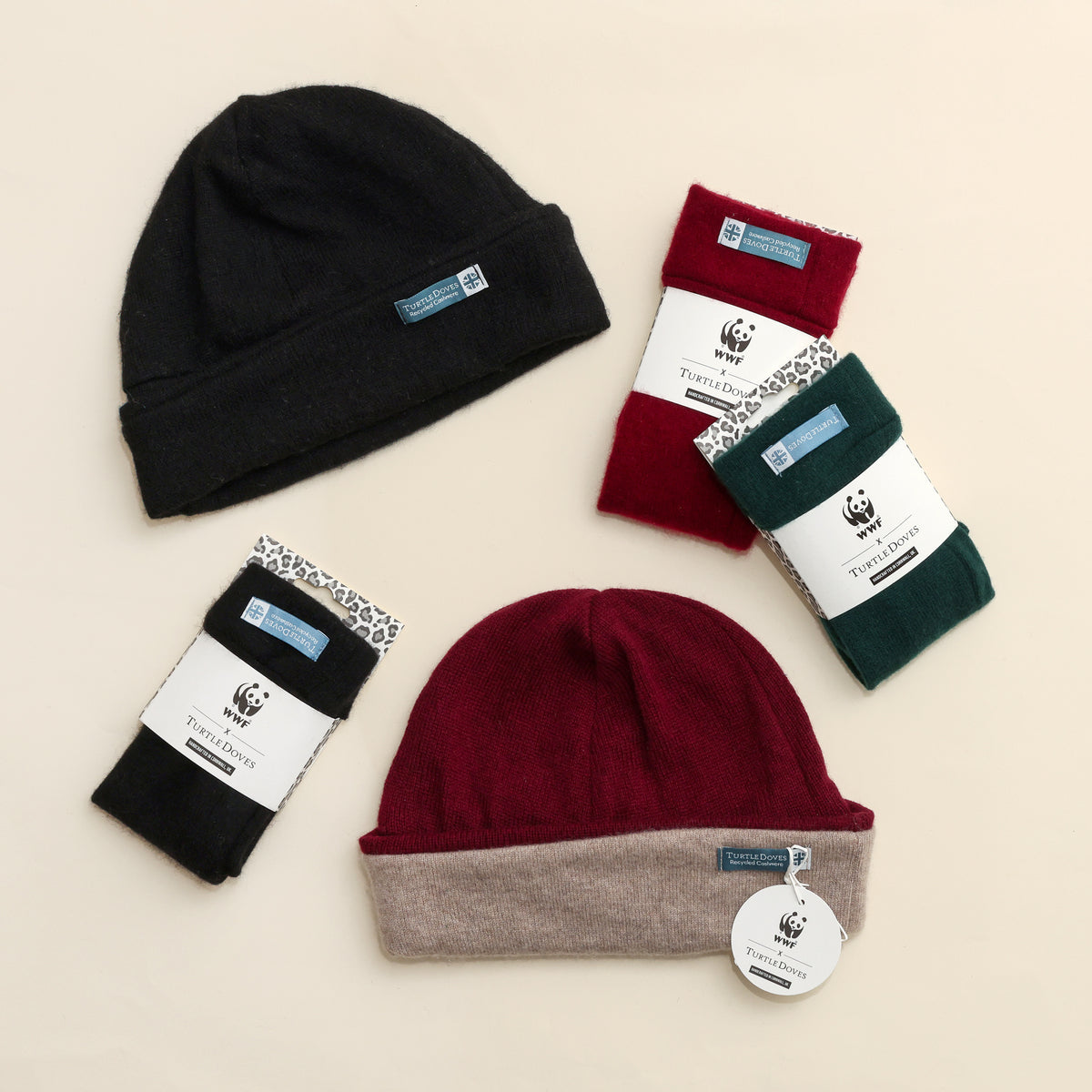 Recycled fingerless gloves with matching recycled cashmere beanies in black and berry with co-branded packaging on cream background