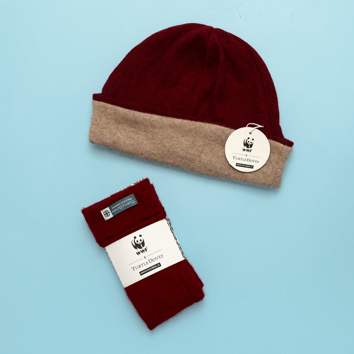 Close up of the beanie and fingerless gloves in berry, showing the co-branded WWF packaging on a blue background
