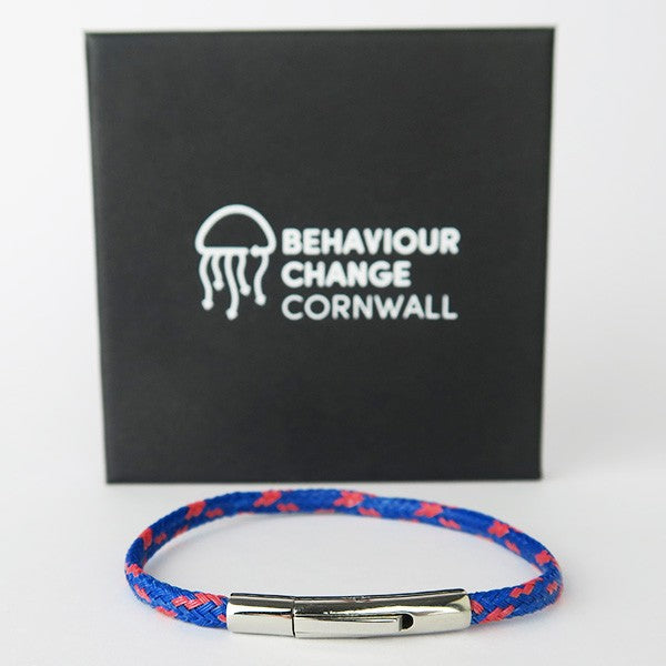 Close up of bracelet in front of Behaviour Change Cornwall gift box, black with white text on white surface