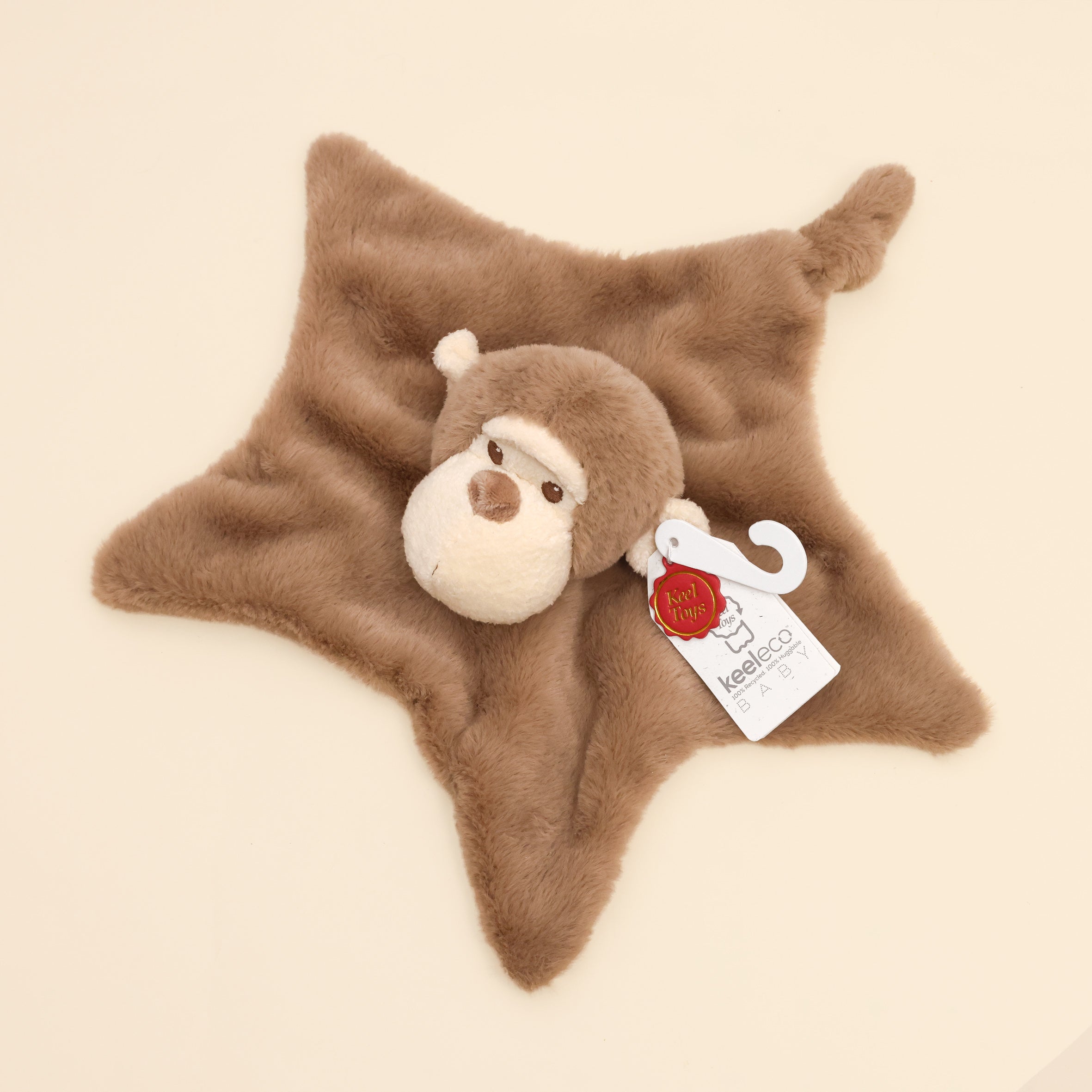 Close up of Baby Marcel Monkey Blanket from above, with KeelECO label and monkey head detail on top. On cream surface
