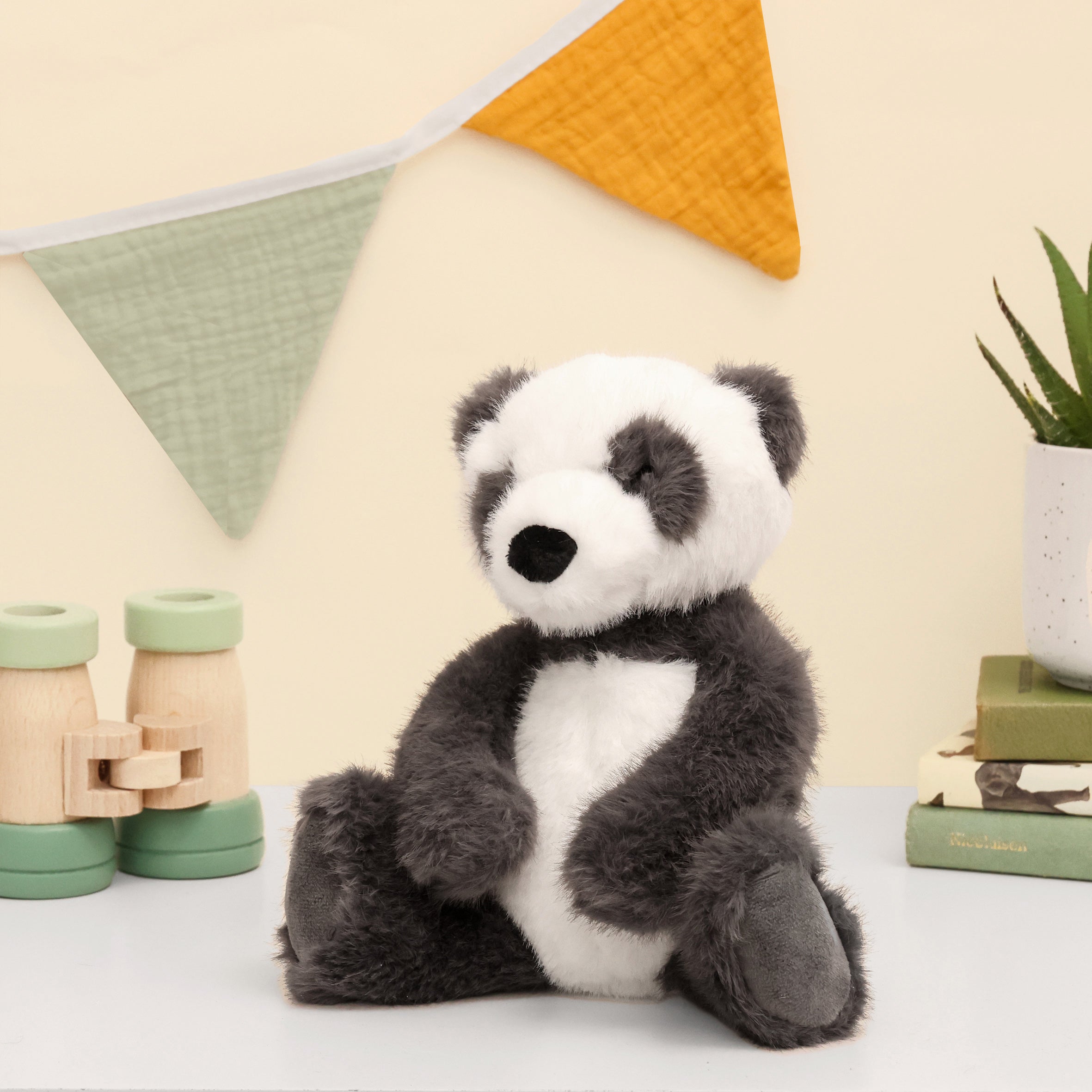 Left side of Panda plush made from recycled plastic bottles sitting on white surface with toys and bunting on the wall