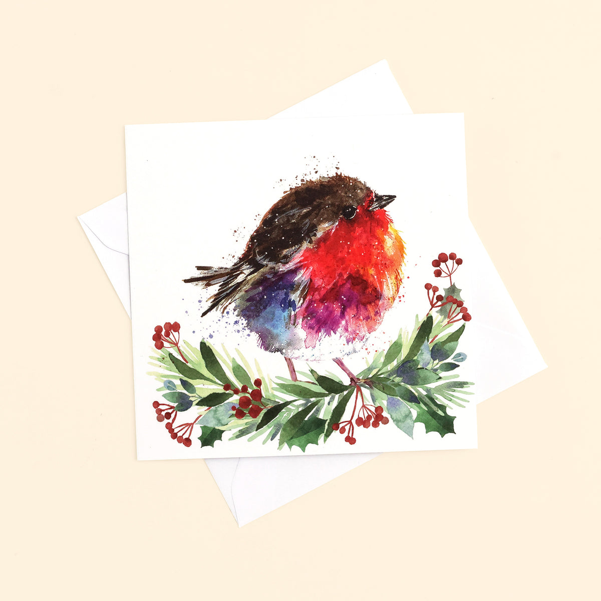 Close up of one of the beautifully illustrated design of a robin sitting on a foliage garland on white background. Card and envelope is on cream surface