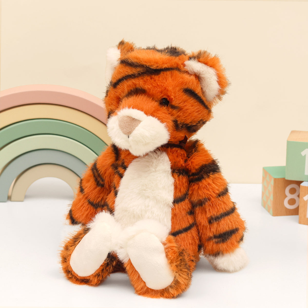Left side of Tiger plush made from recycled plastic bottles. Sitting next to wooden blocks and rainbow on white surface and 