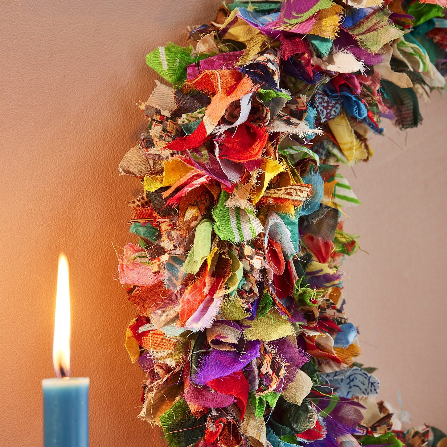 close up of patterned recycled sari fabric in a mix of colours on wreath hanging on terracotta wall next to lit candle