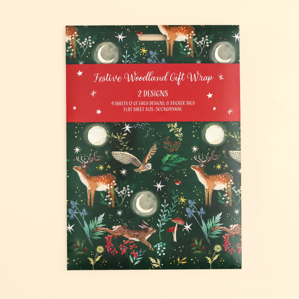 Close up of the festive woodland gift wrap pack on front with illustrated woodlands design in dark green with 4 sheets and 8 sticker tags on cream surface