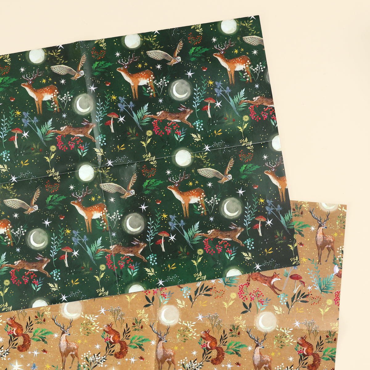 Close up of 2 woodlands designs; one with illustrated deer, owls and hare on dark green background and the other design is a fox, stag and red squirrel on a craft brown background, both in forests with plants, mushrooms, stars and moons