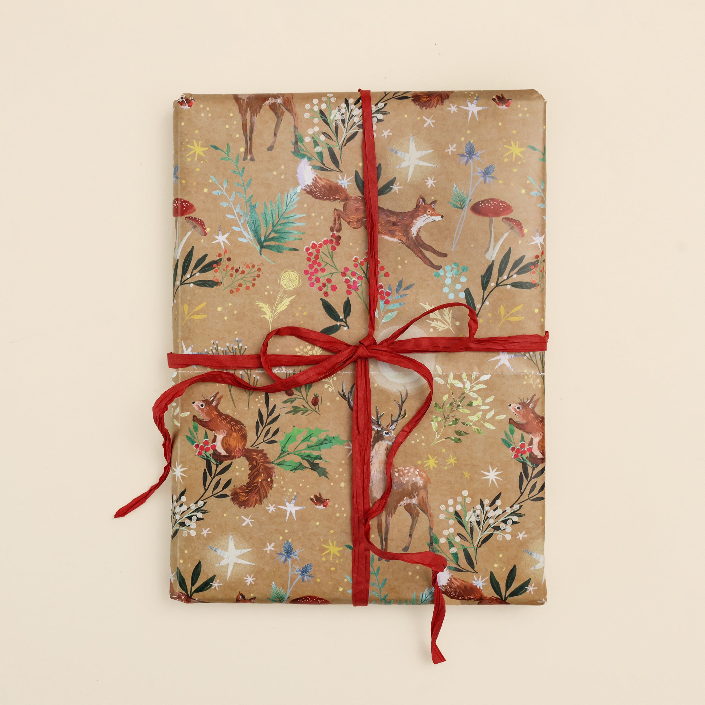 Festive woodlands wrap in craft brown wrapped around a gift with red raffia on cream surface