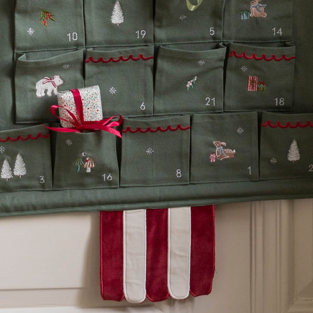 Close up of bottom half of Advent with embroidered numbers, polar bear, deer, trees and mushrooms with red and cream striped stem hanging down on wall.