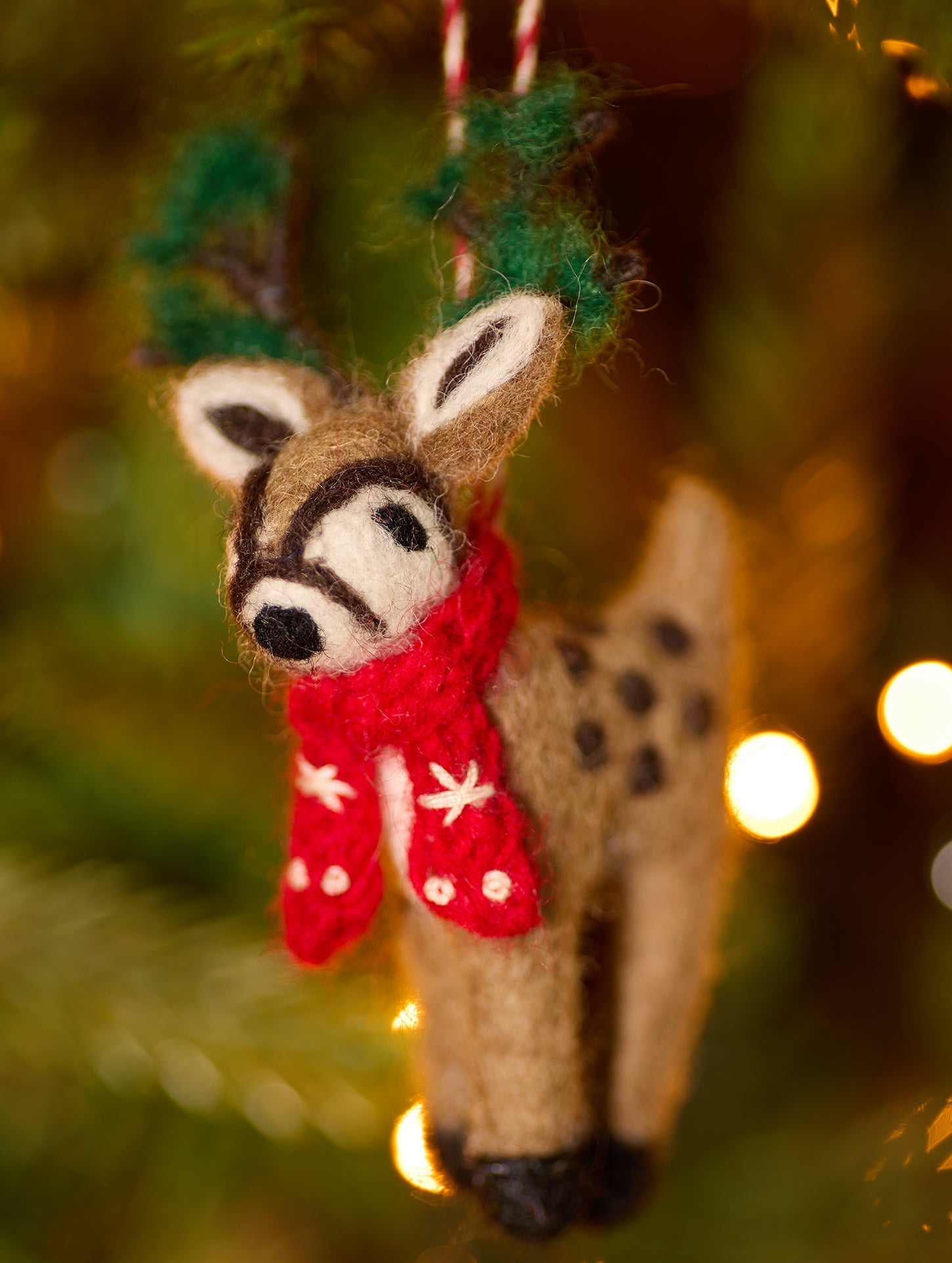 Slight side angle on embroidered felt reindeer decoration showing spotted back hanging on tree with lights
