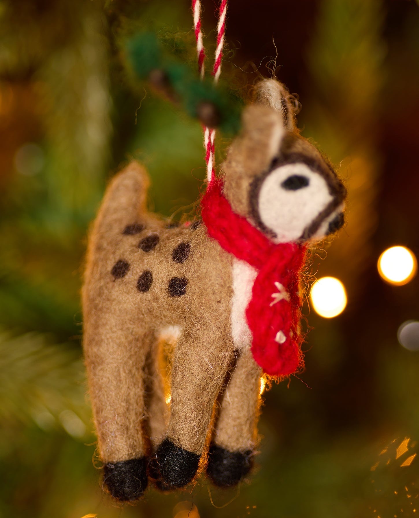 Other side of felt reindeer decoration showing spotted back and black hoofs, face detail, green antlers and red scarf hanging on tree