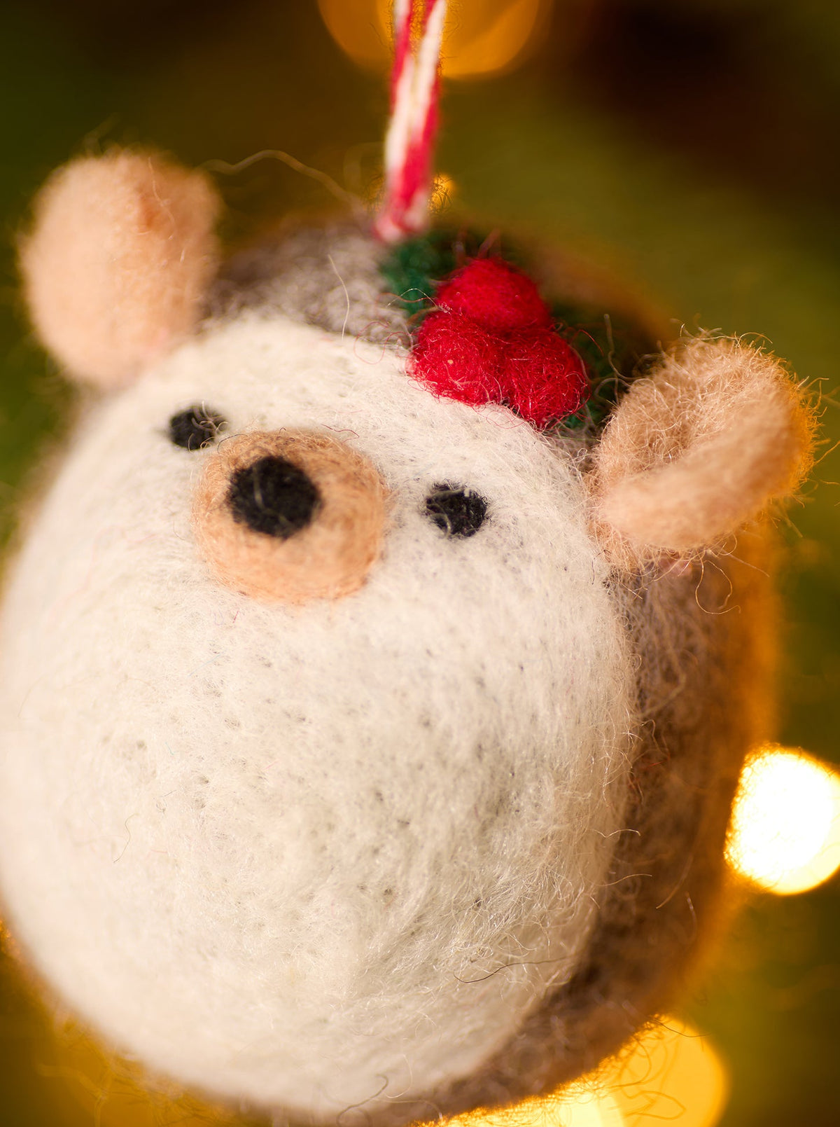 Close up of Felt hedgehog face with holly berries and leaves on the top of the head. Hanging in tree with lights