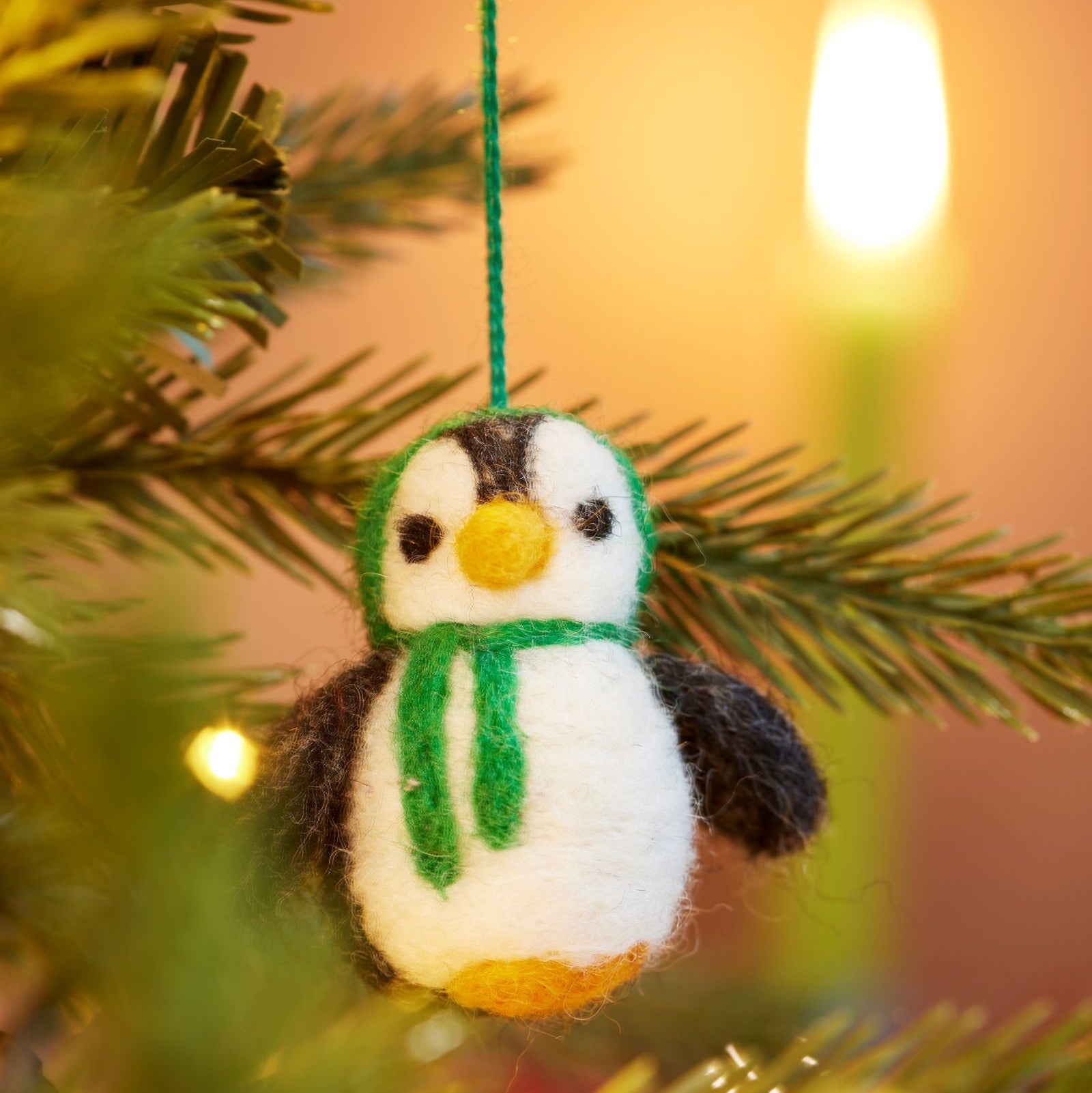Close up of handmade felt penguin decoration with Green hood and scarf hanging in tree with lights