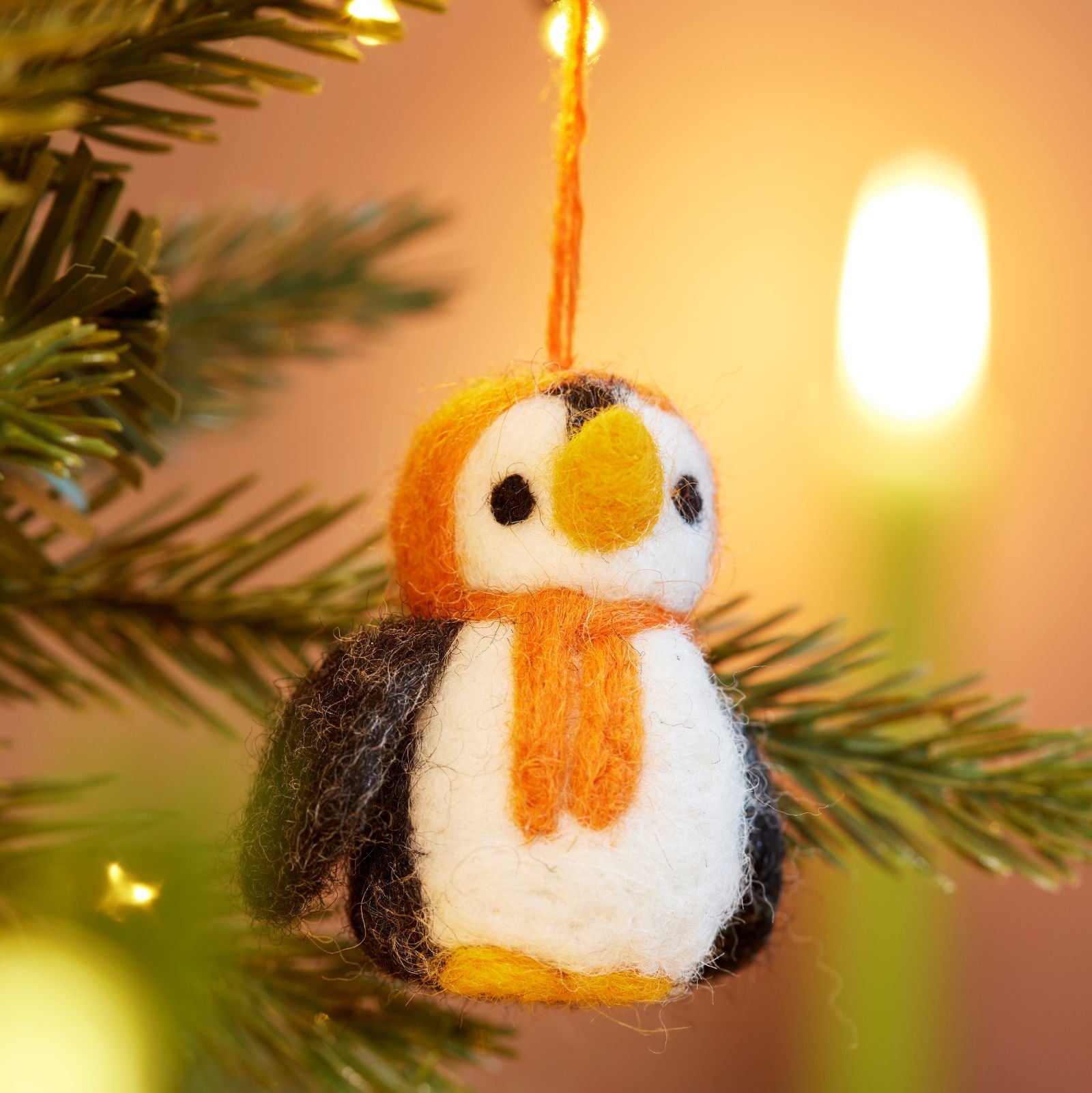Close up of handmade felt penguin decoration with Orange hood and scarf hanging in tree with lights