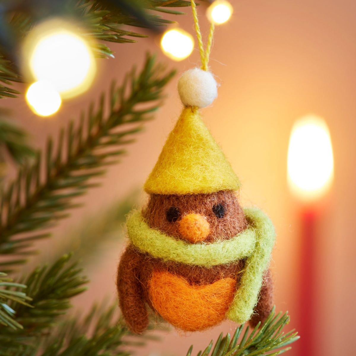 Close up of felt orange robin with yellow bobble hat and lime green scarf hanging in tree with lights
