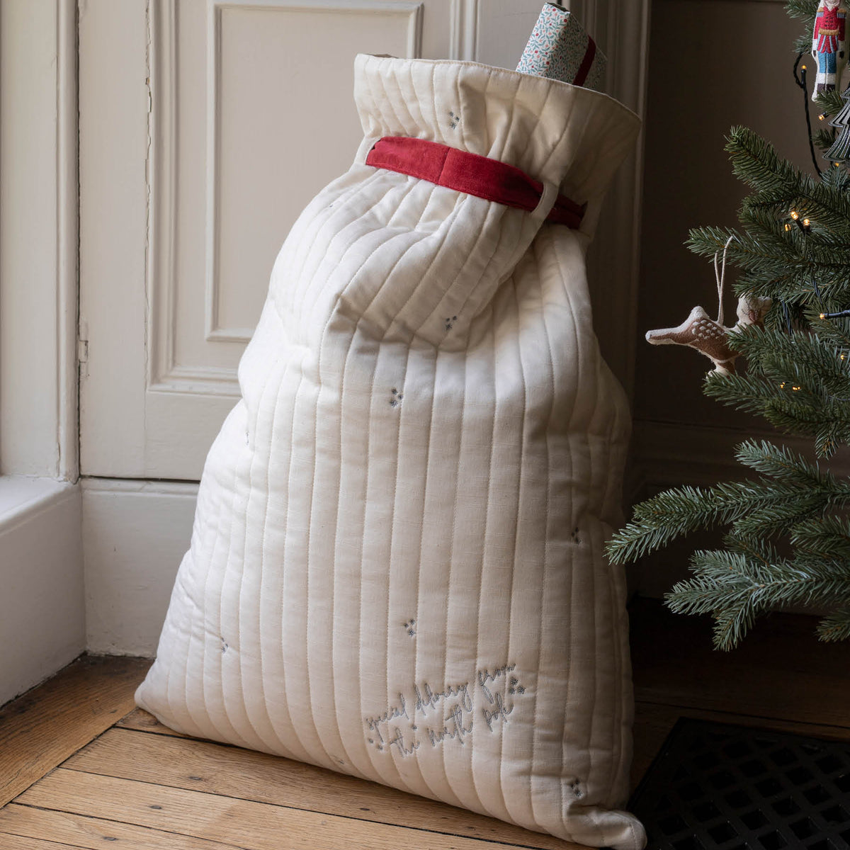 Reverse of filled present sack with embroidered message next to decorated Christmas tree