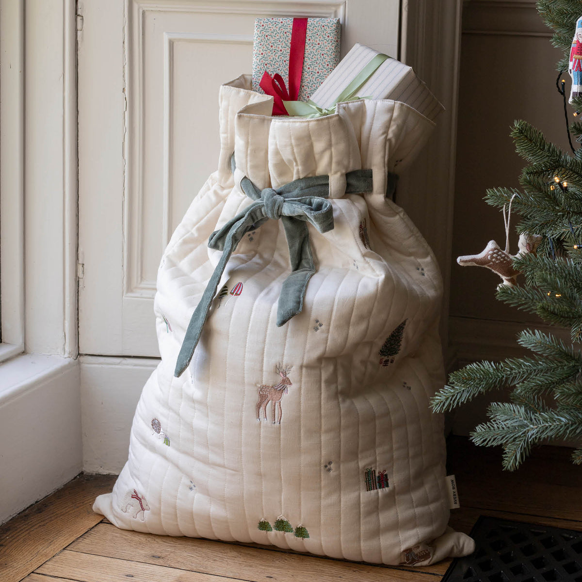 Cotton Embroidered Christmas sack with presents inside next to a tree and window