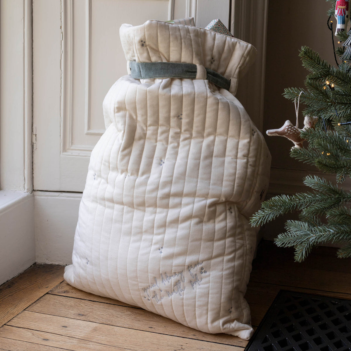Reverse of filled Cotton present sack with green velvet ribbon next to decorated Christmas tree