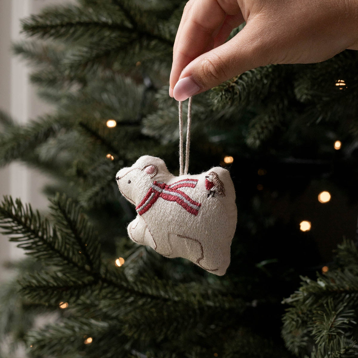 Cotton embroidered Polar bear Christmas decoration being held in front of a lit Christmas tree